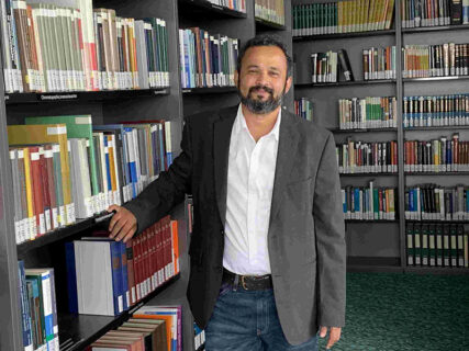 Portrait von Prof. Dr. Halmuthur M. Sampath Kumar, der vor einem Regal mit Büchern steht.