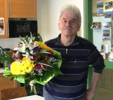 Prof. Dr. Frasch in seinem Büro. Er hat einen Blumenstrauß mit gelben Blumen in der Hand, den er zu seinem Abschied erhalten hat.