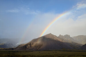 Das Foto zeigt eine Berglandschaft mit einem doppelten Regenbogen im Himmel.