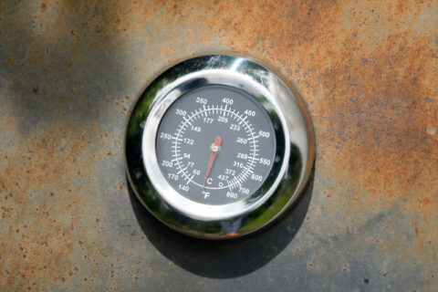 Ein rundes Thermometer liegt auf einer rostigen Oberfläche.