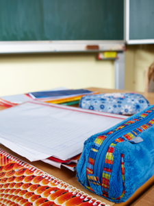 Das Foto zeigt einen Ausschnitt aus einem Klassenzimmer. Im Hintergrund sieht man eine Tafel. Im Vordergrund sieht man einen Tisch, auf dem mehrere Blöcke und ein Federmäppchen liegen.