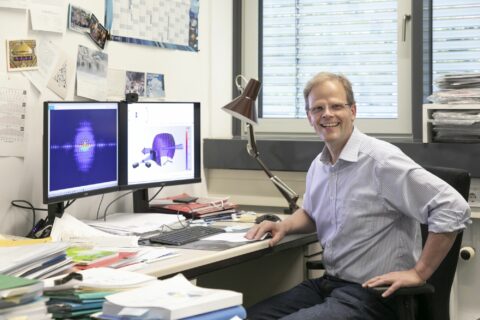 Prof. Dr. Joachim von Zanthier sitzt in seinem Büro am Computer. Er lächelt in die Kamera.
