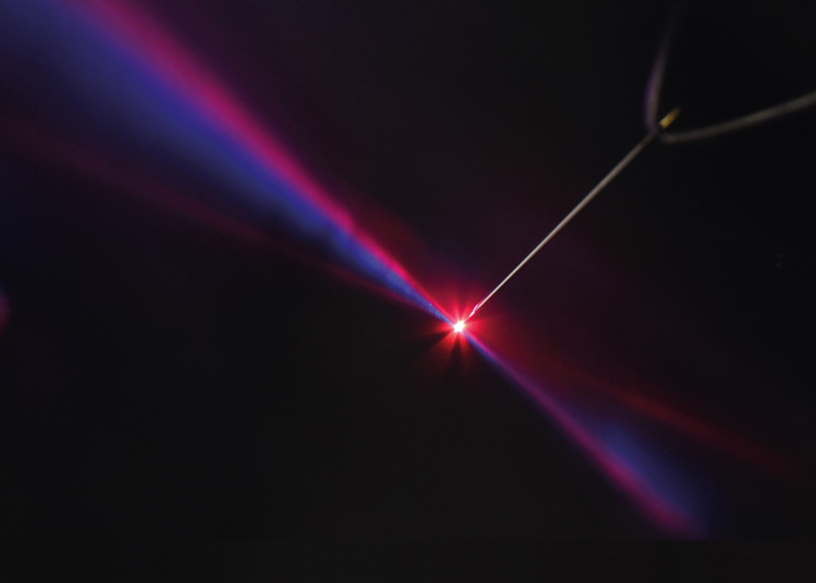Ein starker Laserpuls (im Foto rot) wird mit einem Puls der doppelten Lichtfrequenz (blau) überlagert. Beide Pulse werden über einen Parabolspiegel (links) auf eine Metall-Nadelspitze fokussiert. Die emittierten Elektronen (nicht sichtbar) werden entsprechend ihrer Energie detektiert. Eine Wiederholung dieser Messung mit unterschiedlichem, zeitlichem Versatz der Felder erlaubt es, auf das Emissionszeitfenster zurückzuschließen. (Bild: FAU/Tobias Boolakee, Philip Dienstbier)